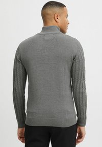Grauer Pullover mit hohem Kragen und strukturiertem Zopfmuster an den Ärmeln. Glattes Material und gerippte Bündchen sowie Saum.
