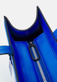 Sininen nahkalaukun sisustus, jossa on sileä pinta, pyöristetyt reunat ja keskellä hopeavetoketju mustalla vetolapulla.