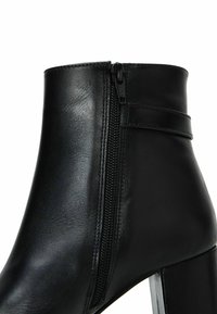 Bottine en cuir noir avec fermeture éclair latérale, talon épais et silhouette épurée. Texture lisse avec des accents matériels minimaux.