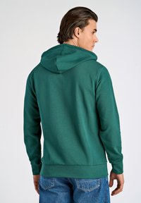 Felpa verde con cappuccio e finitura testurizzata, maniche lunghe e polsini a coste. Vista posteriore, abbinata a jeans blu.