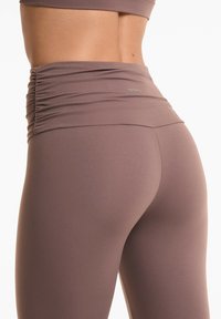 Leggings mauve cu talie înaltă, fabricate din material elastic, având detalii plisate la talie și o textură netedă. Logo vizibil.