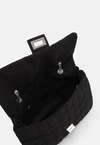 Borsa a tracolla nera trapuntata con tessuto testurizzato, hardware in argento e chiusura magnetica. L'interno presenta una tasca con zip e una fodera liscia.