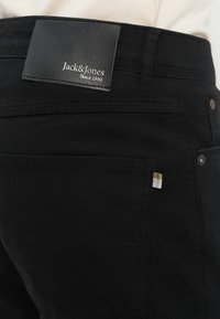 Μαύρα τζιν από τζιν ύφασμα με υφή δερμάτινης ετικέτας που φέρει τη σήμανση "Jack & Jones". Διαθέτουν τσέπη με υφασμάτινη λεπτομέρεια πλέξης.