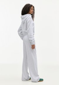 Lichtgrijze, cropped hoodie met een capuchon, gecombineerd met brede sweatpants. Zacht materiaal met ribbekanten; model staat met de hand op de heup.