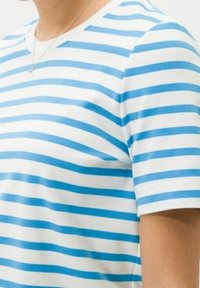 Sininen ja valkoinen raidoitettu t-paita, joka on valmistettu puuvillasta. Paidassa on pyöreä kaulus ja lyhyet hihat. Raidat ovat tasaisesti sijoitettuja, luoden siistin ilmeen.