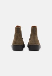 Ruskotaiset nahkasaappaat, joissa on sileä pinta, pyöreä kärki ja musta kumipohja. Takana on pieni suorakaiteen muotoinen etiketti.