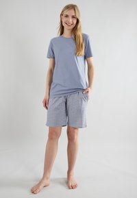 T-shirt azzurro chiaro a maniche corte abbinato a pantaloni corti a quadri blu e bianchi, dotati di tasche laterali e dalla vestibilità comoda.