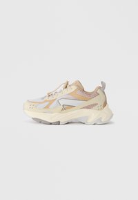 Sneaker aus einer Mischung von beigem, cremigem und grauem Mesh- und Synthetikmaterial, mit einer strukturierten Sohle und dekorativen Nähten.