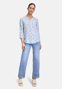 Blusa blu con motivo e scollatura a V; abbinata a jeans larghi blu chiaro con orlo ricamato. Il modello indossa scarpe con tacco beige.