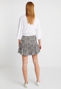 Falda corta floral con dobladillo en volantes, hecha de tejido ligero con un estampado de leopardo en blanco y negro. Detalle en la cintura ceñida.