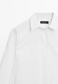 Chemise blanche à manches longues en coton, avec un col classique, un devant à boutons et un design minimaliste sans motifs visibles.