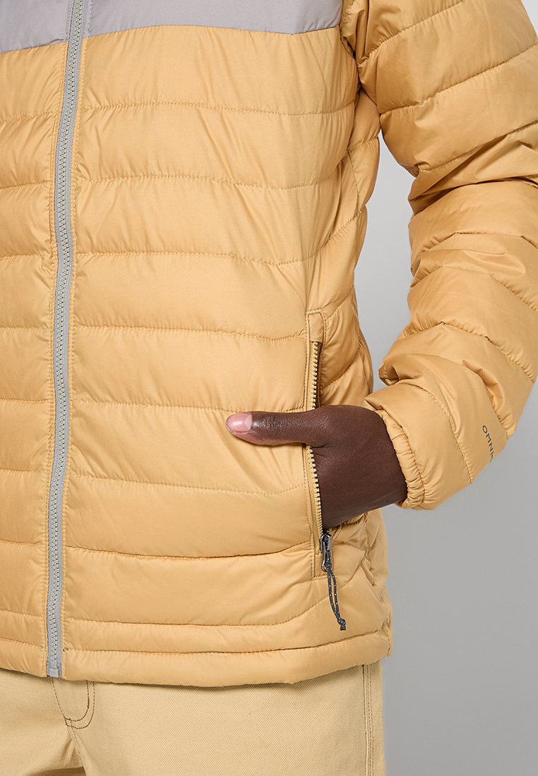 Żółta kurtka puchowa z jasnoszarym yoke, poziomym pikowaniem, zapinanymi na zamek kieszeniami bocznymi oraz elastycznymi mankietami. Miękki, lekki materiał.