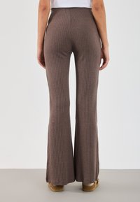Brown ribbed flared pants with a high waist, featuring vertical stripes and a textured knit finish, paired with brown platform shoes.