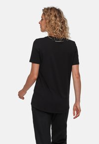 Sort kortærmet T-shirt lavet af blød bomuld, med en buet kant og et lille logo på ryggen. Enkel, minimalistisk design.