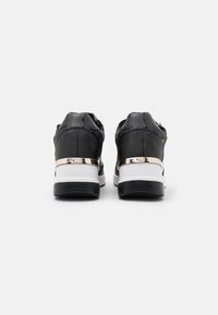 Black sneakers with glossy material, featuring a textured back, metallic silver accents, and a white midsole. Sports design with modern styling.