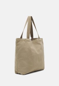 Beige lerret tote bag med to solide stoffhåndtak, rektangulær form og myk tekstur. Ingen synlig logo eller ytterligere detaljer.