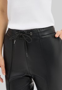 Pantalons en cuir noir avec une taille élastique à cordon et des accents en métal argenté, présentant une texture lisse et un design ajusté.