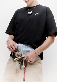 Sort bomulds T-shirt med korte ærmer, beige denimbukser med en synlig blåstribet talje og tilbehør hængende fra bæltet.