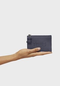 Portefeuille en cuir marine avec finition texturée, logo "TOUS" embossé, fermeture zippée et un porte-bonheur ours gris attaché.