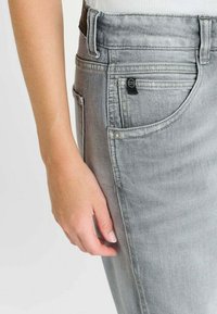 Grijze denim jeans met een smalle pasvorm, zichtbare stiksels en een voorzak. De stof heeft een licht versleten textuur en een zwart logolabel.