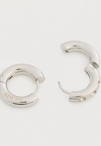 Ασημένια σκουλαρίκια κρίκοι με γυαλιστερή φινίρισμα, με τρεις μικρές διάφανες ρουμπίνες από τη μια πλευρά και σχέδιο κλειδώματος με μεντεσέ.