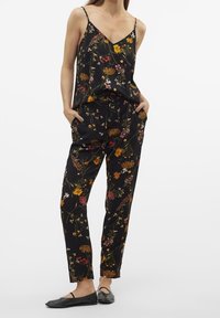Černý květovaný overal s výstřihem do V, tenkými ramínky a volnými kalhotami s kapsami. Materiál má hladkou, měkkou strukturu.