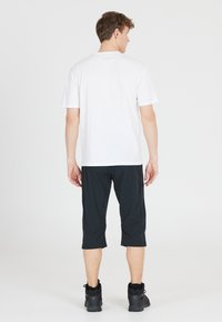 Valkoinen lyhythihainen T-paita, yhdistetty mustiin polvenpituisiin housuihin. Kangas näyttää sileältä; housuissa on sivusaumat ja taskut. Mustat kengät viimeistelevät asun.