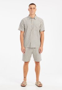 Camisa de botones de manga corta y pantalones cortos a juego en color beige claro con rayas verticales oscuras. Presenta un bolsillo en el pecho y un corte relajado.