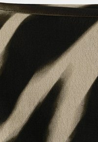 Imagine de aproape cu o țesătură bej cu forme abstracte mari negre și o margine sau tiv de culoare maro închis de-a lungul părții superioare.