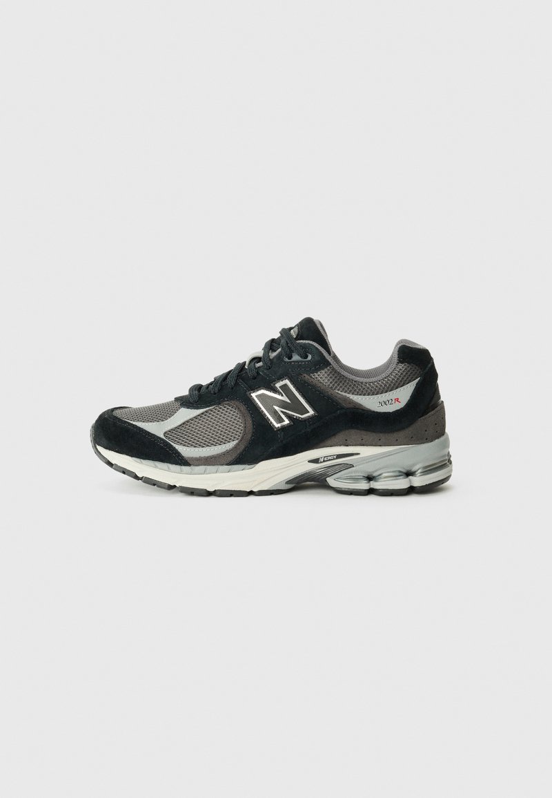 Chaussure de sport noire et grise avec des matériaux en mesh et en suédine, à bout rond, fermeture à lacets et semelle rembourrée avec des accents de talon notables.