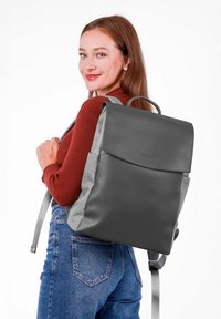 Šedý kožený a šedý textilní batoh s vrchním klopou a ramenními popruhy. Obsahuje rukojeť a logo na přední straně. Minimalistický design.