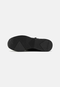 Svart gummiyttersåle med et teksturert mønster, som har spor og rygger for godt grep. Glatt finish med subtil merkevarerdetalj.
