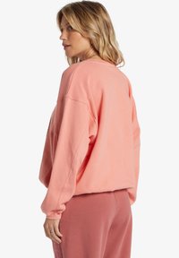 Sweat-shirt corail surdimensionné avec un col rond, des épaules tombantes et des poignets côtelés, associé à un pantalon de détente rose assorti.