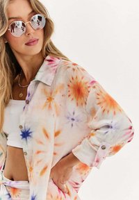 Farebná tričko s technikou tie-dye vyrobené z ľahkého materiálu, so vzormi v oranžovej, ružovej a modrej farbe, s gombíkovým zapínaním a vyhrnutými rukávmi.