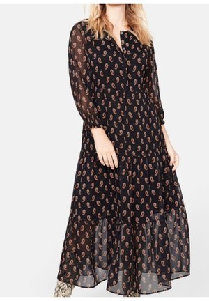 Schwarzes Kleid mit langen Ärmeln aus schichtweise transparentem Stoff, der ein wiederkehrendes beige Paisleymuster aufweist und einen Knopfkragen hat.