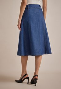 Mørkeblå denim A-linje-skjørt med synlige sømmer, flagrende kant og midilengde. Brukt med svarte slingback hæler.