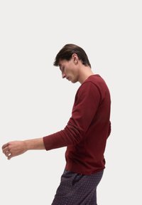 Long-sleeve maroon shirt made of cotton, featuring a crew neck and fitted sleeves. Paired with patterned pajama bottoms with blue dots.