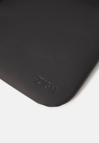 Svart, matt yta med präglad "ZIGN"-bokstäver, med rundade kanter och mjuk textur. Minimalistisk design betonar enkelhet.