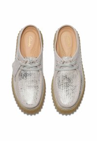 Light gray slip-on shoes with a metallic textured upper, round toe, gray laces, and a chunky tan rubber sole.