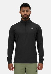 Haut de sport noir à manches longues avec fermeture éclair, doté d'un col montant et d'un petit logo réfléchissant sur la poitrine gauche. Tissu doux avec une texture lisse.