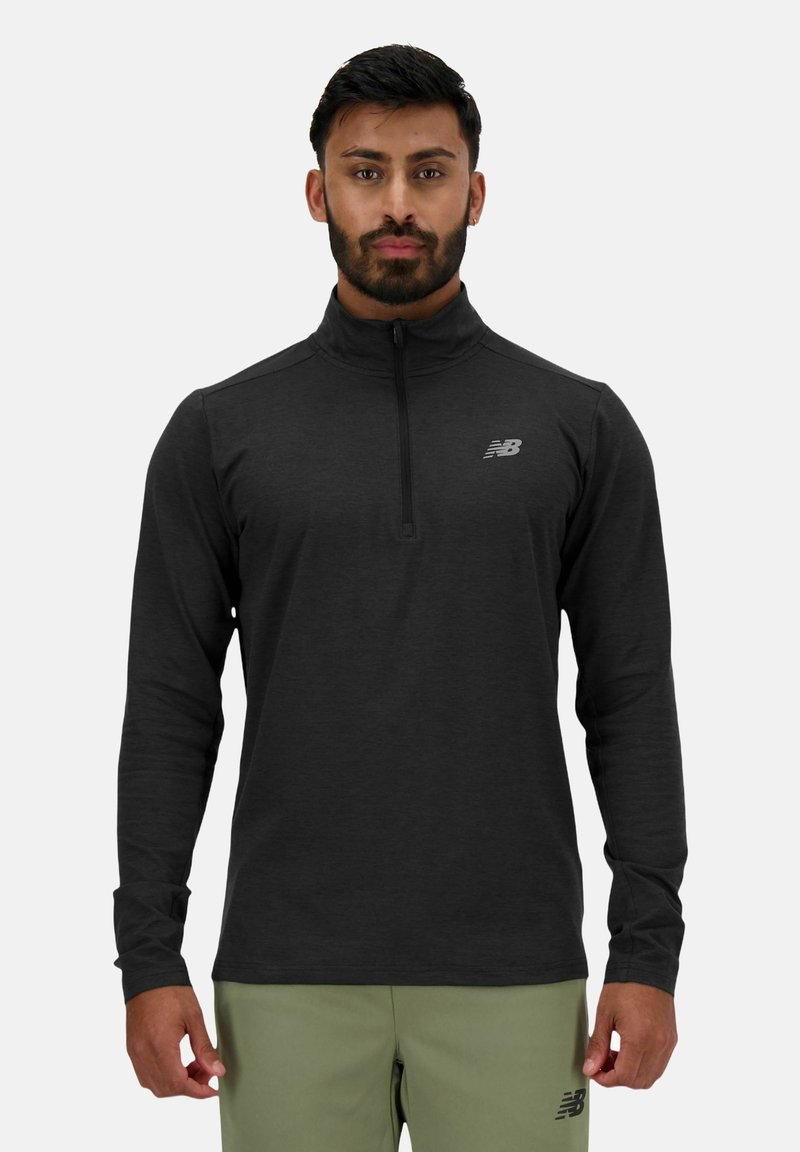 Haut de sport noir à manches longues avec fermeture éclair, doté d'un col montant et d'un petit logo réfléchissant sur la poitrine gauche. Tissu doux avec une texture lisse.