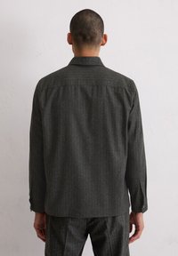 Ciemnoszara koszula z długim rękawem z pionowymi paskami, mankietami na guziki i klasycznym kołnierzem, wykonana z teksturowanej tkaniny. Widok od tyłu.