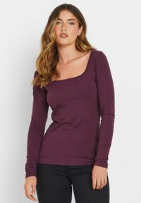 Pitkähiha, istuva paita syvän purppuranvärisestä puuvillasta, jossa on neliön muotoinen pääntie ja saumatonta hihoja. Materiaali näyttää pehmeältä ja joustavalta.