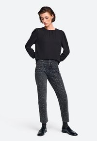 Zwarte blouse met lange mouwen en een ronde hals, gecombineerd met donkergrijze jeans met verspreide zilveren versieringen. Zwarte schoenen.