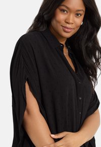 Svart knäppskjorta med korta ärmar, med en strukturerad tyg med subtila mönster och en avslappnad passform.