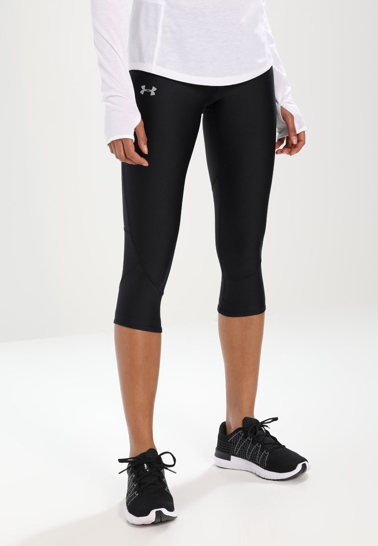 Czarne legginsy capri wykonane elastycznego materiału, o dopasowanym kroju z detalami szwów. W zestawieniu z czarnymi butami sportowymi.