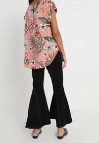 Rosa blommig topp med korta ärmar, med vita och gröna mönster, kombinerad med svarta utsvängda byxor och platta skor.