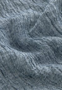 Tissu bleu texturé avec un motif ondulé, présentant une surface douce et légèrement en relief. Le matériau semble léger et flexible.