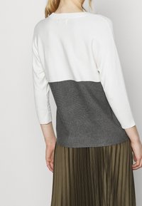 Maglione lavorato a maglia con una parte superiore bianca e una parte inferiore grigio scuro, maniche a tre quarti e una vestibilità rilassata.