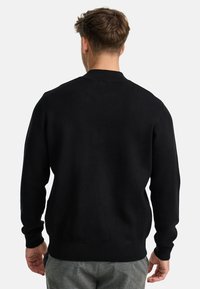 Mustahdodd black nuttu, tohveliga, pikkade varrukatega, soonikute mansettide ja äärega, millel on sile tekstuur ja minimalistik disain.